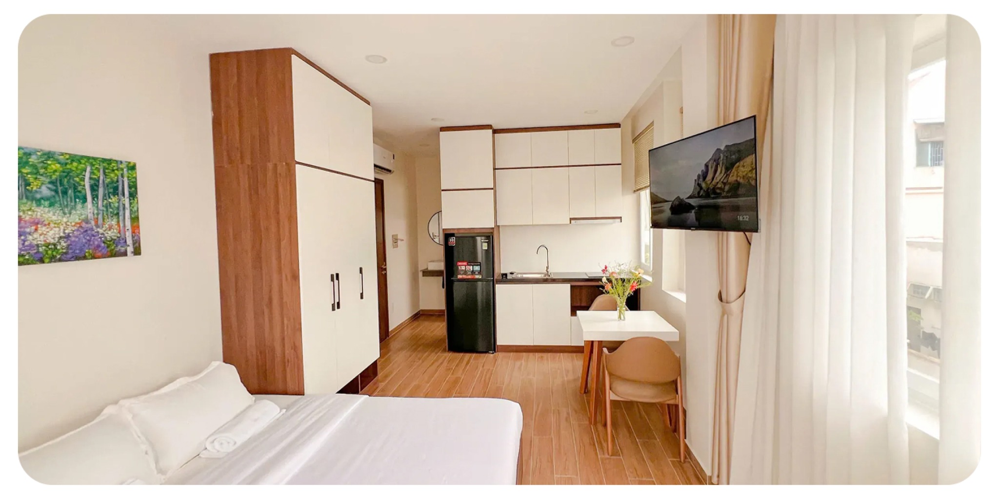 Khu bếp hiện đại tủ lạnh, tủ kệ, b&agrave;n ăn nhỏ với hoa tươi, giường ngủ drap trắng, kh&ocirc;ng gian mở tho&aacute;ng đ&atilde;ng của căn hộ Heyday Apartment