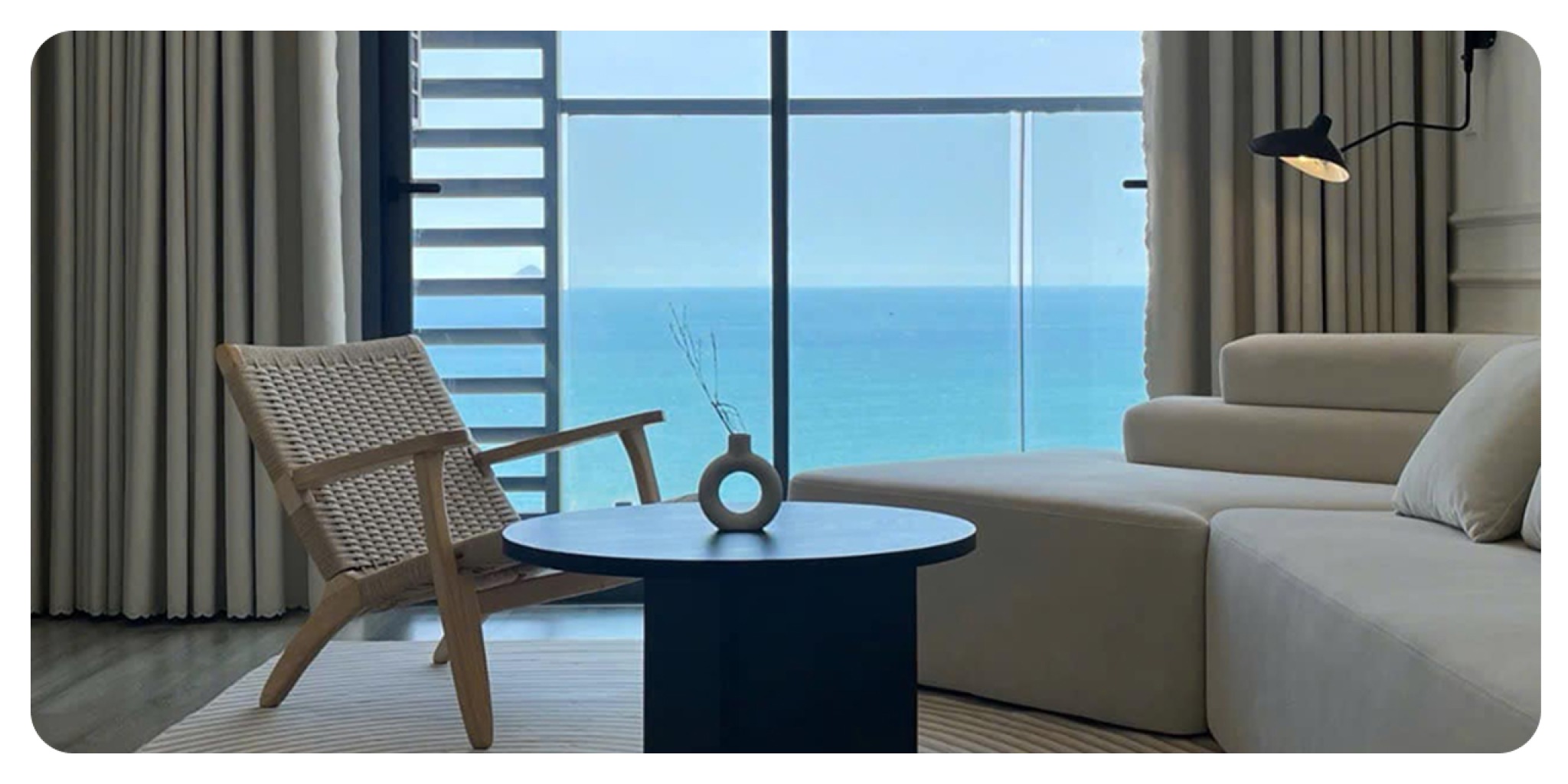 Cửa sổ kính lớn với view biển từ Serenity View Nha Trang Phòng khách căn hộ Serenity View với cửa sổ kính trần, rèm sáng màu và tầm nhìn toàn cảnh biển Nha Trang, mang lại nhiều ánh sáng tự nhiên.