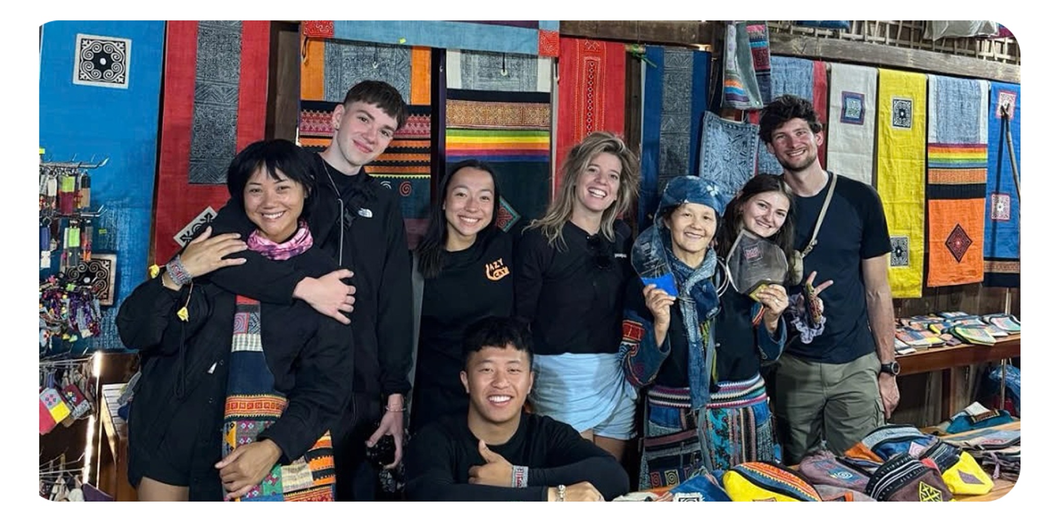 Nh&oacute;m du kh&aacute;ch quốc tế của Lazy Cat Homestay đang tham quan v&agrave; mua sắm c&aacute;c sản phẩm thổ cẩm địa phương trong kh&ocirc;ng gian chợ truyền thống H&agrave; Giang, thể hiện m&ocirc; h&igrave;nh homestay kết hợp tour du lịch trải nghiệm.